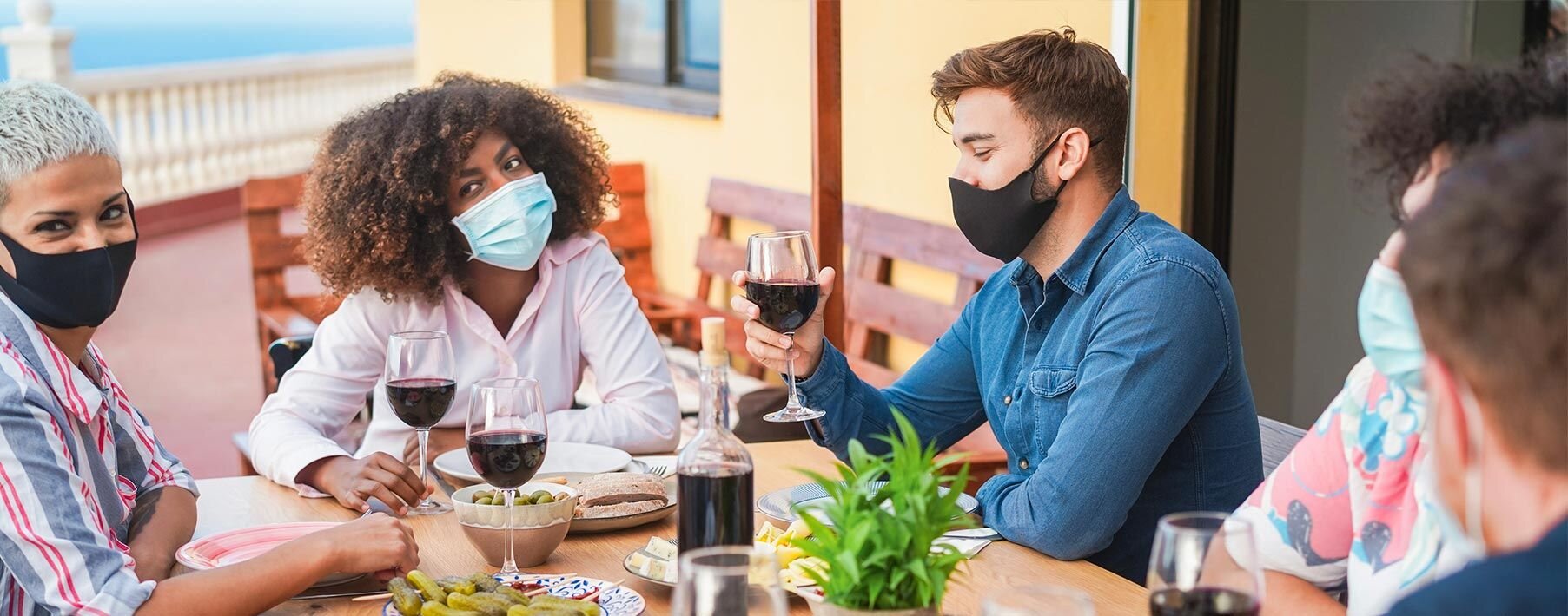 A group of people in masks at a dinner table holding glasses of wine