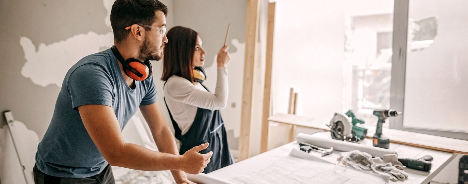 A man and a woman looking out a window with tools and paint around them