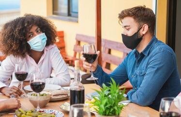A group of people in masks at a dinner table holding glasses of wine