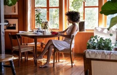 A woman writing at a desk by a window with plants around her