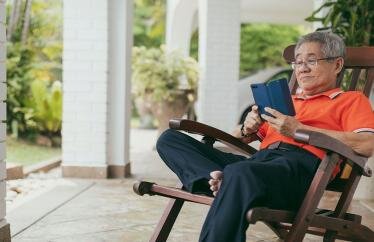 An older man reading his phone on a rocking chair on a front porch
