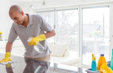 A man cleaning a kitchen counter with a cloth wearing yellow gloves
