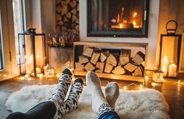 Close up of two homeowners' feet wearing socks and resting on a cozy rug in front of a fireplace